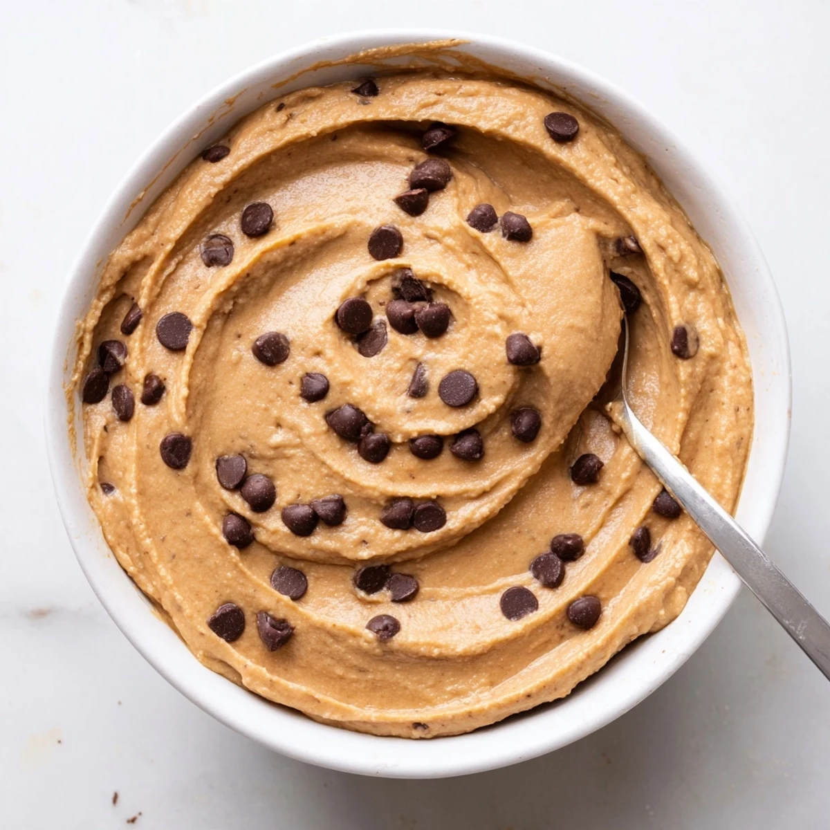 A bowl of creamy Chocolate Chip Cookie Dough Hummus ready to be scooped with fruit or crackers.