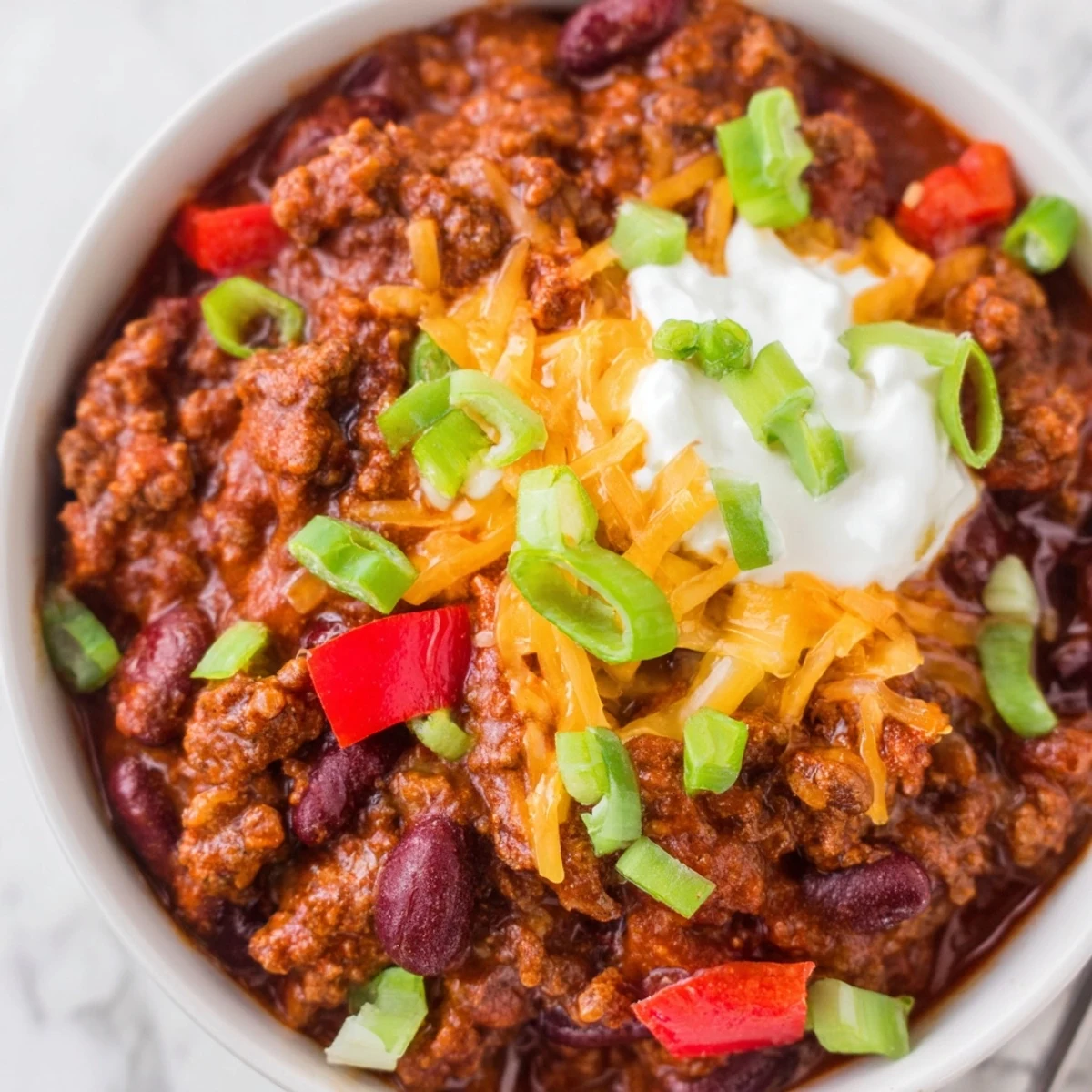 Steaming beef and bean chili with sharp cheddar melts into a rich, red tomato base in a rustic Dutch oven.