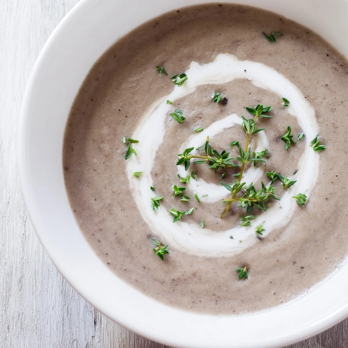 Creamy Mushroom Soup with thyme is ladled from a rustic pot into a white bowl.