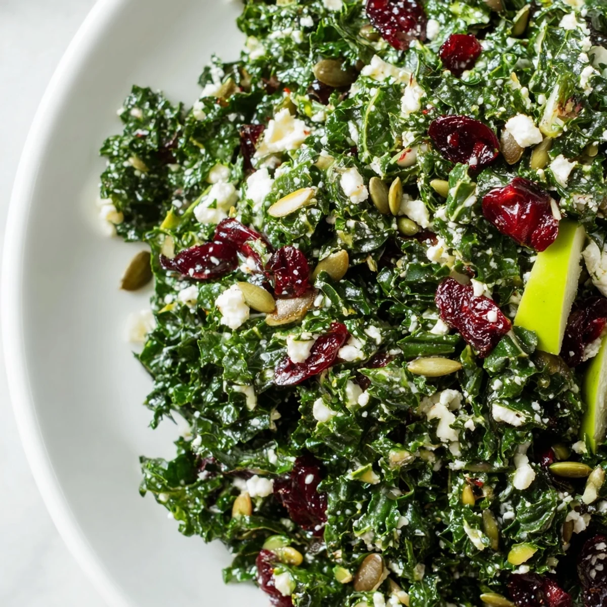 Freshly massaged Winter Kale Salad with cranberries and pepitas is tossed in a bright citrus dressing. Served in a white bowl for a healthy, festive winter lunch.