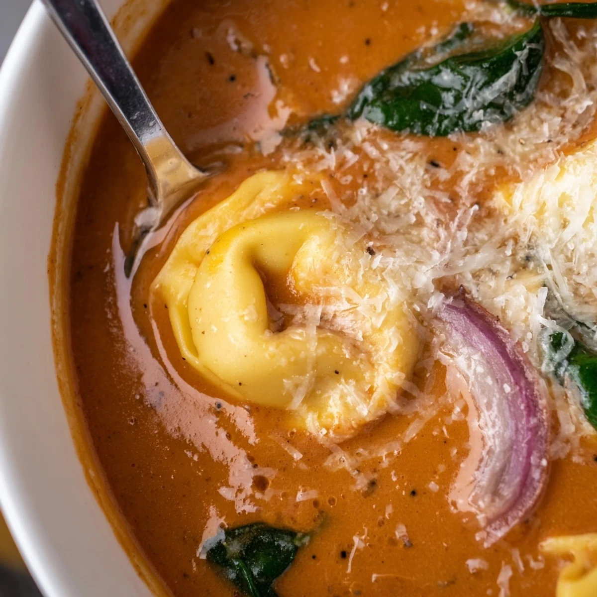 Creamy Tomato and Tortellini Soup with Spinach in a rustic bowl with steam rising beside crusty bread.
