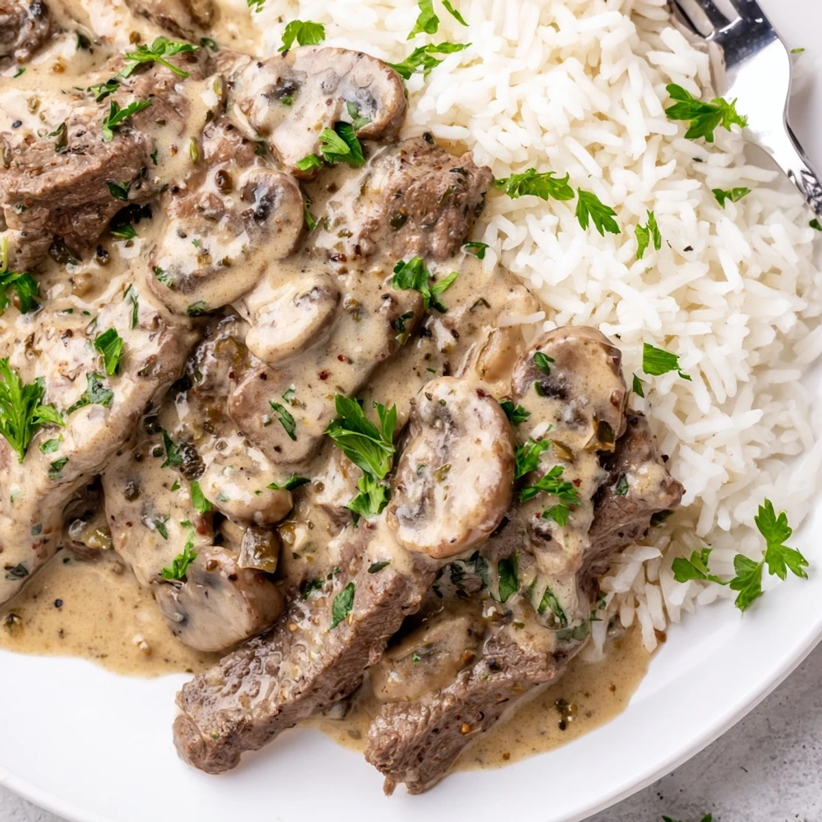 Golden Beef Stroganoff with Basmati Rice piled high with creamy mushroom sauce and parsley garnish.