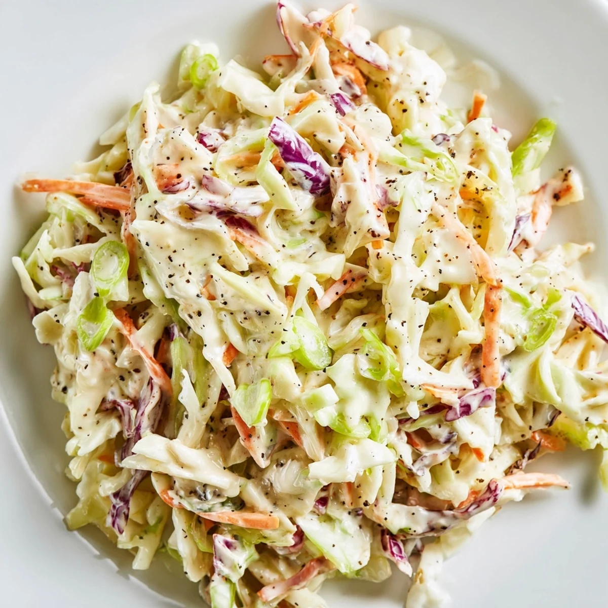Plate of Creamy Coleslaw with Carrots garnished with green onions, served chilled alongside a grilled sandwich.