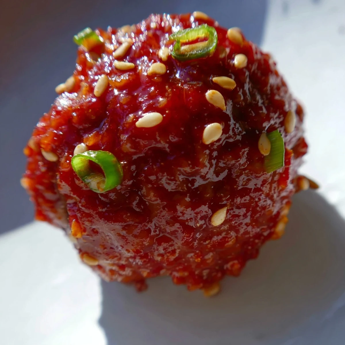 Crispy baked Spicy Sriracha Beef Meatballs glisten with a sweet and spicy glaze, garnished with fresh green onions and sesame seeds. 