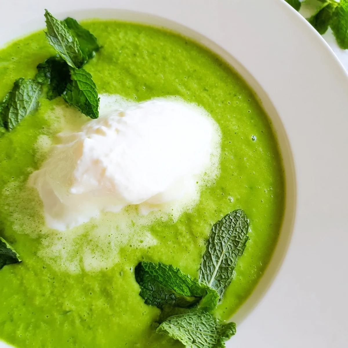 Creamy Green Pea and Mint Soup served hot, garnished with crème fraîche and a sprinkle of black pepper.  