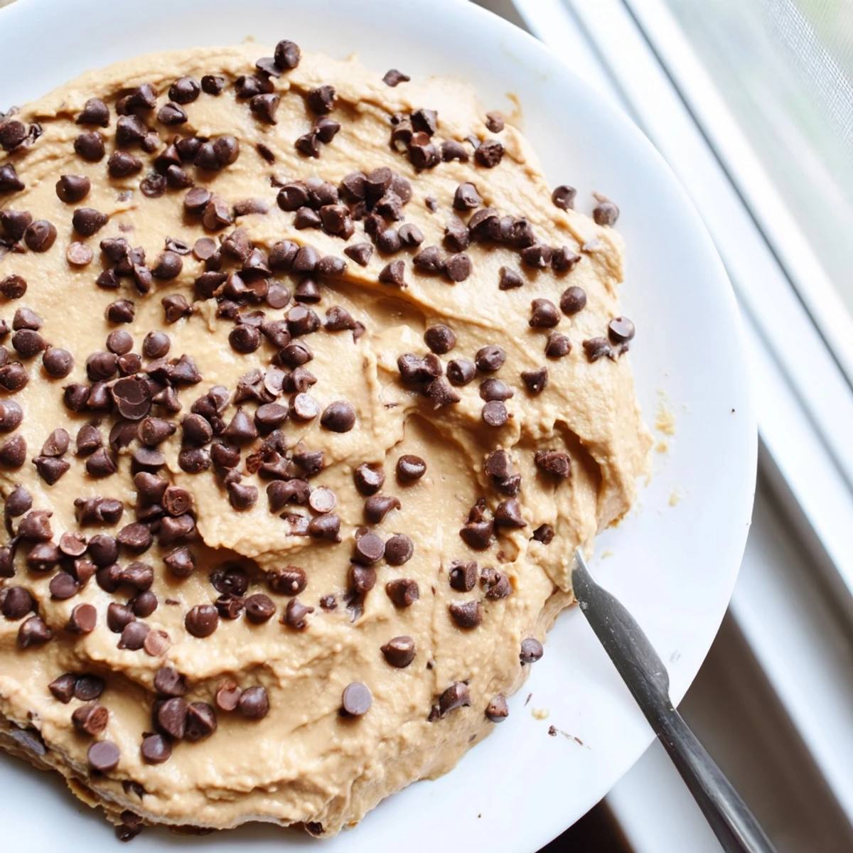 A creamy, sweet chocolate chip cookie dough hummus served in a rustic bowl with dippers on the side.