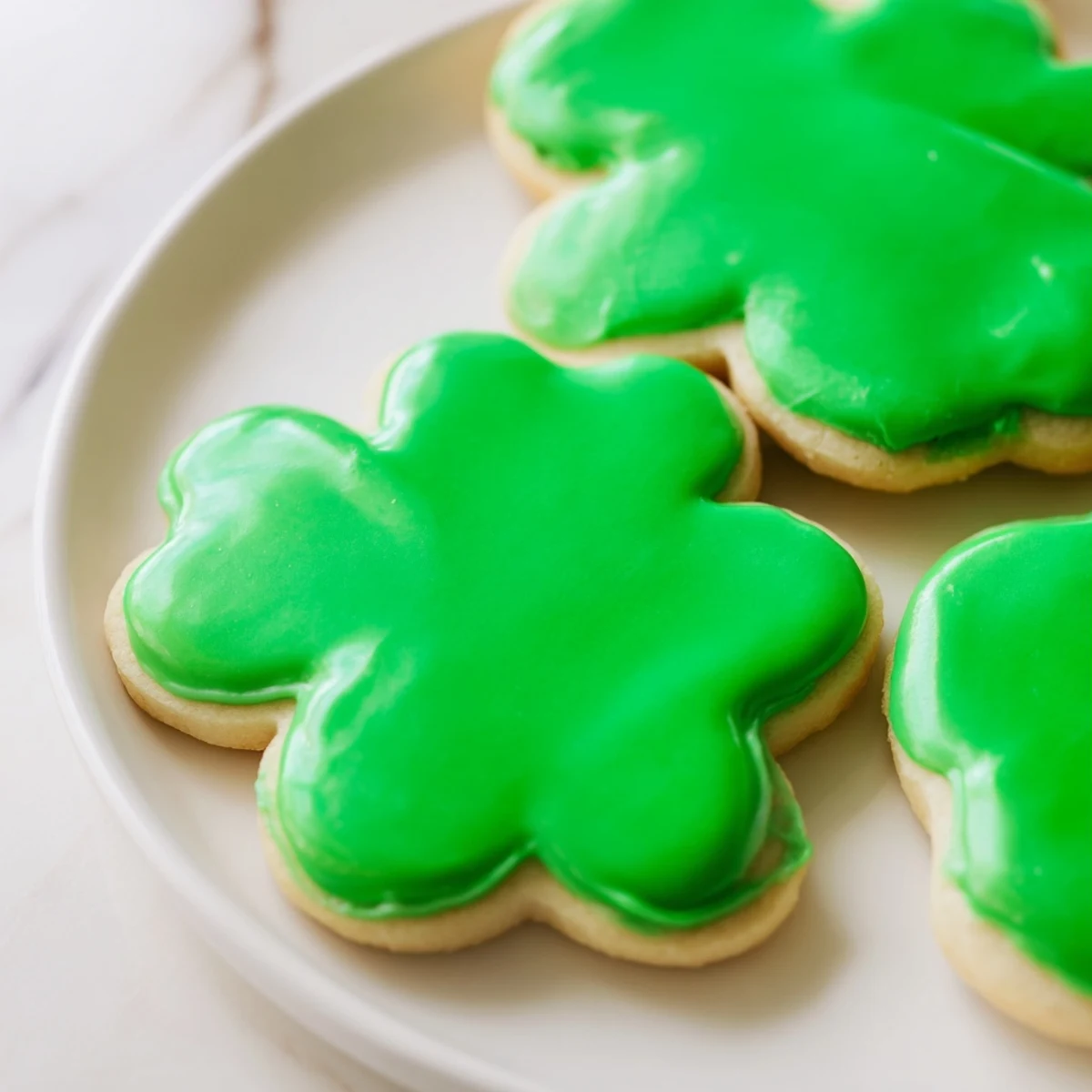 Freshly baked Shamrock Sugar Cookies with green icing are stacked on a wire cooling rack, ready for a festive dessert platter.