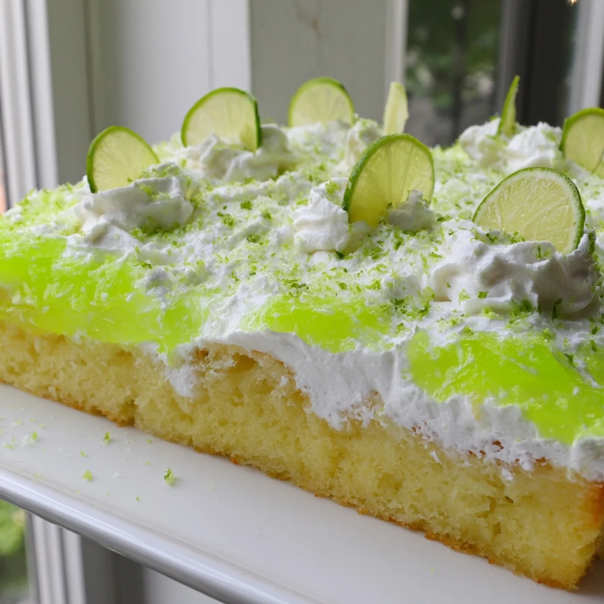 A chilled slice of lime poke cake with fluffy whipped cream topping and fresh lime zest garnish.