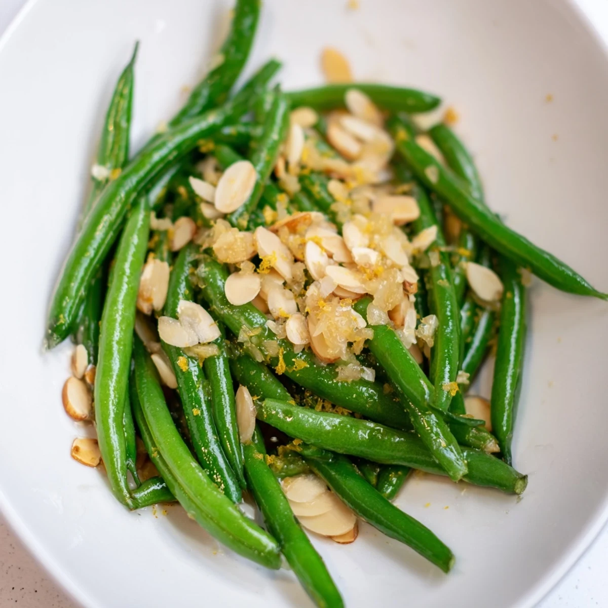 A close-up of green beans with lemon and toasted almonds highlights garlic butter coating and lemony zest aroma.
