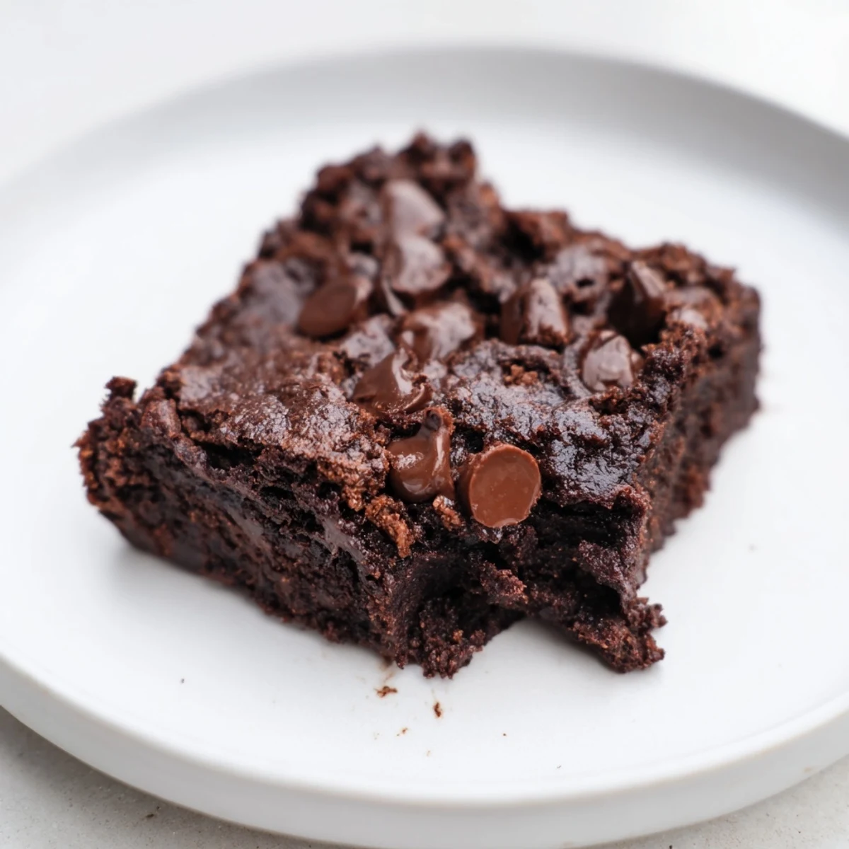 Fudgy gluten-free almond flour brownies on a white plate, melting chocolate chips visible on top and a serving suggestion with vanilla ice cream.