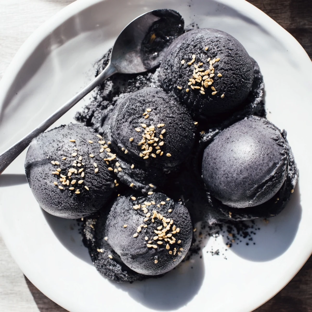 A scoop of toasted black sesame ice cream sits in a ceramic bowl, topped with a sprinkle of seeds.