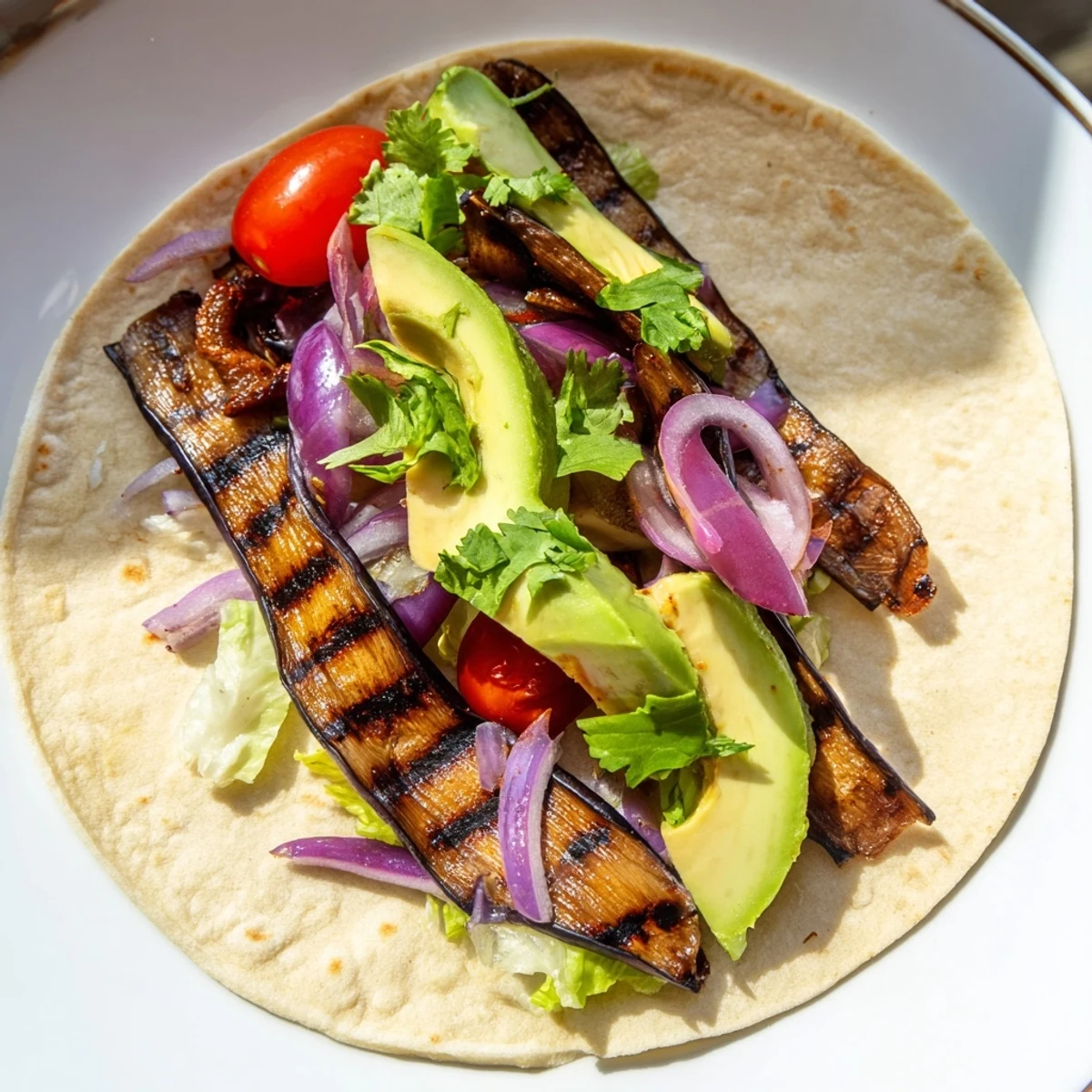 Charred Eggplant Tacos served on warm corn tortillas, topped with fresh lettuce, juicy tomatoes, and creamy avocado slices.