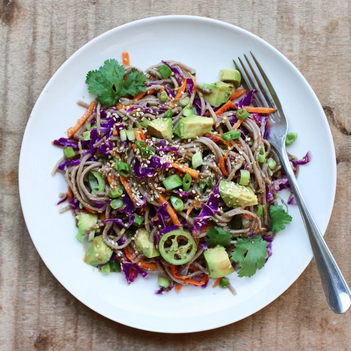 Top-down view of a vibrant Japanese-inspired Sesame Avocado and Soba Noodle Salad with julienned carrots and cucumbers, ready to eat.