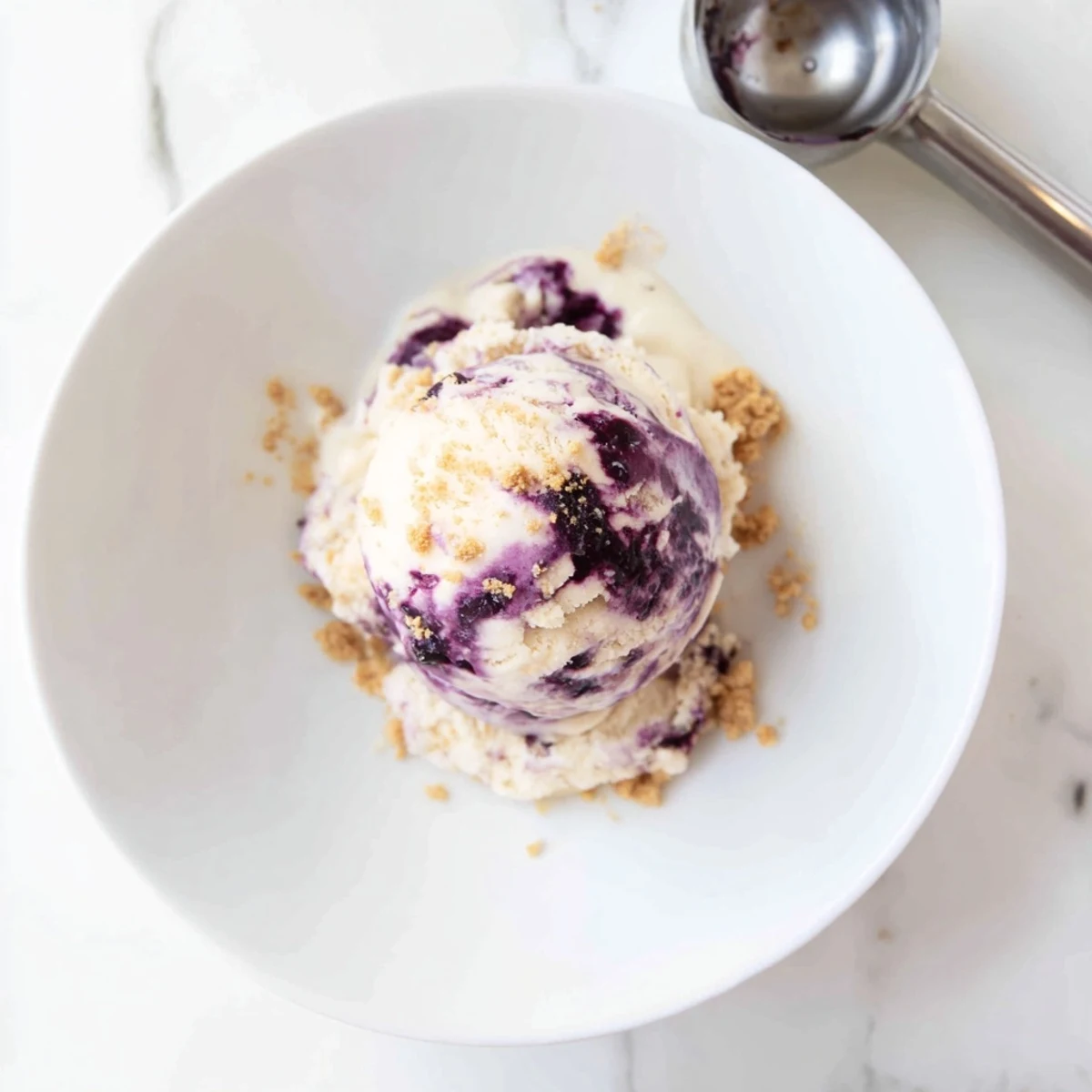 Creamy Lemon Blueberry Cheesecake Ice Cream in a bowl with graham cracker crumbs.