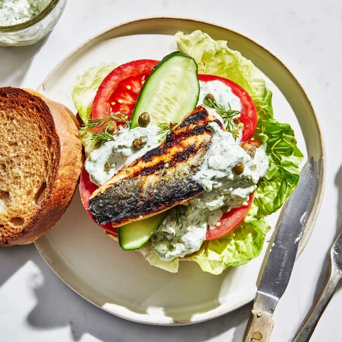 A vibrant burger spread shows barramundi, grilled romaine, and tangy jalapeño tartare, ready to serve with tomato slices.