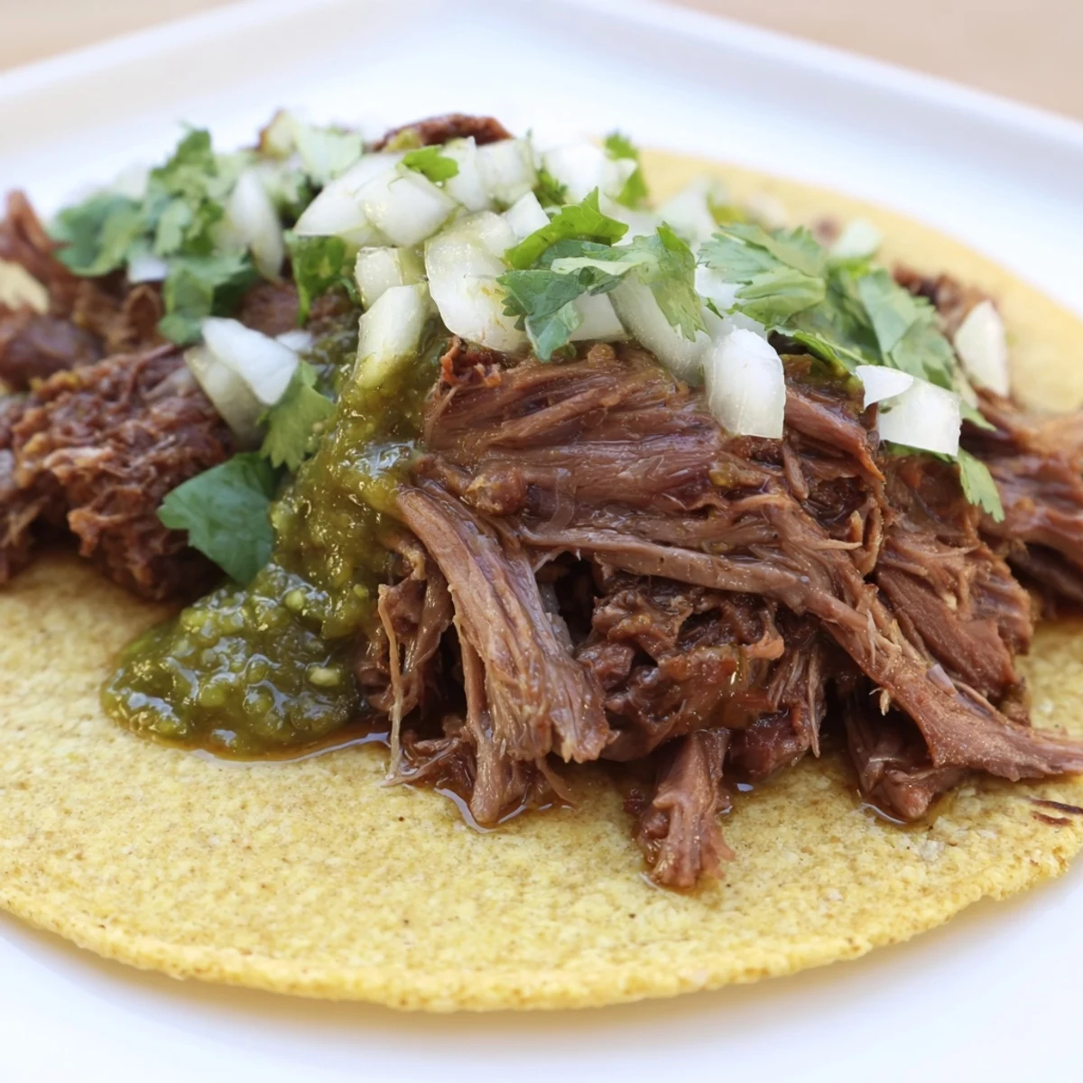 Slow-braised Beef Cheek Tacos are served in warm corn tortillas topped with fresh cilantro and onion.