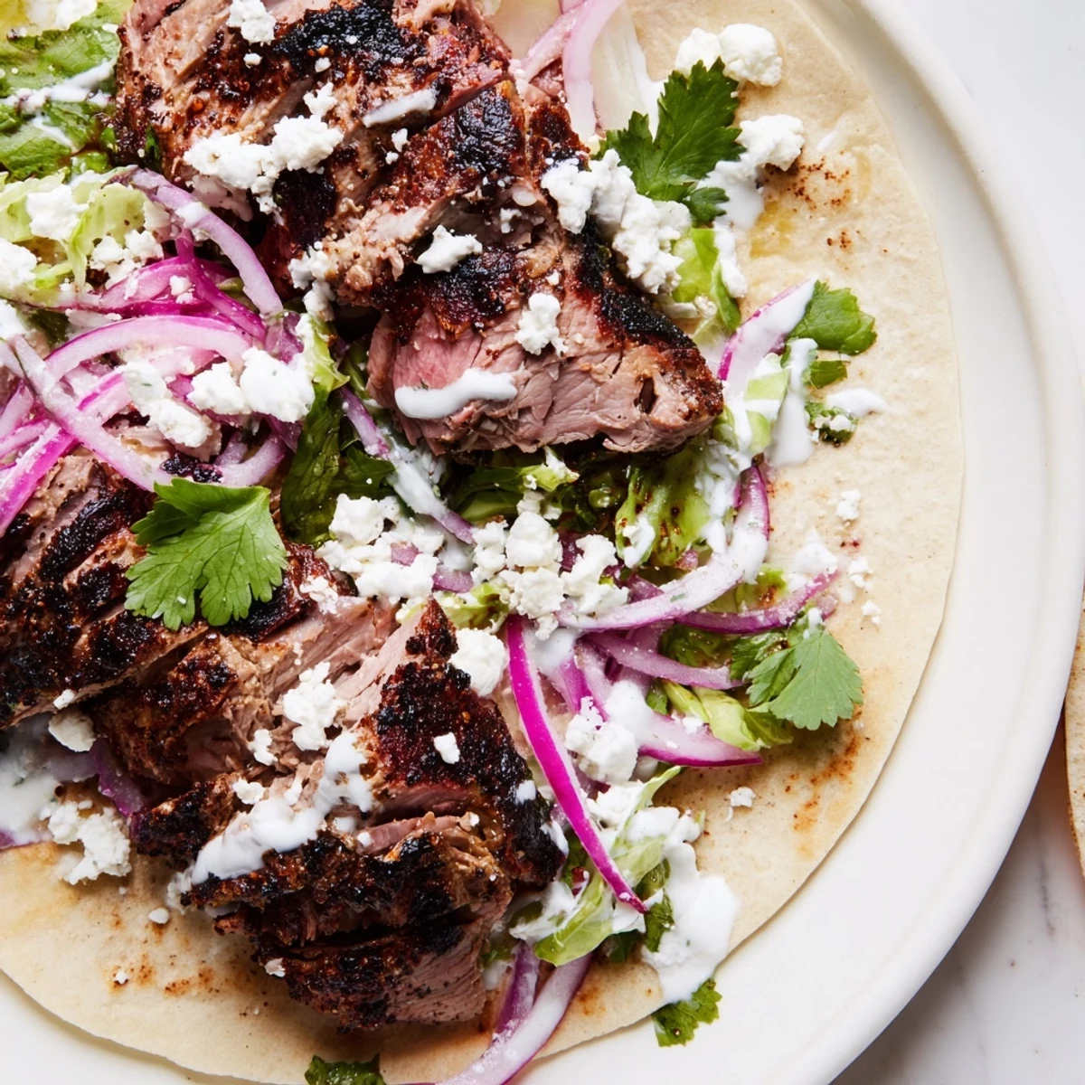 Savory Cumin Crusted Leg of Lamb with Tacos plated beside a bowl of yogurt-lime sauce for dipping.
