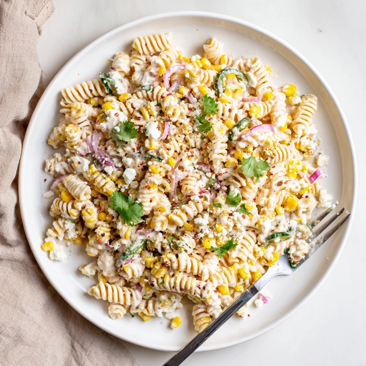 Vibrant Mexican Street Corn Pasta Salad served chilled with lime wedges, red bell peppers, and charred sweet corn kernels.