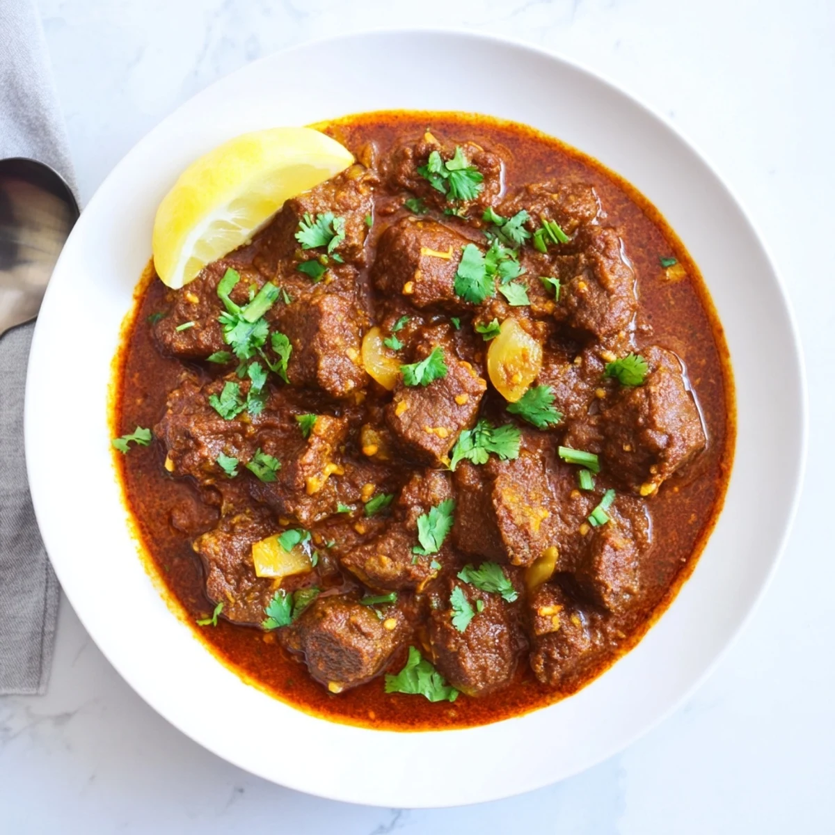 Close-up of Indian Beef Curry with Tomato Gravy in a skillet, topped with fresh cilantro and paired with warm naan bread.