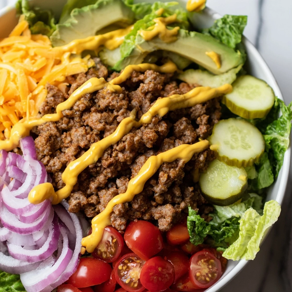 A hearty burger bowl with seasoned ground beef, fresh lettuce, cherry tomatoes, cheddar, pickles, and creamy burger sauce drizzled on top.