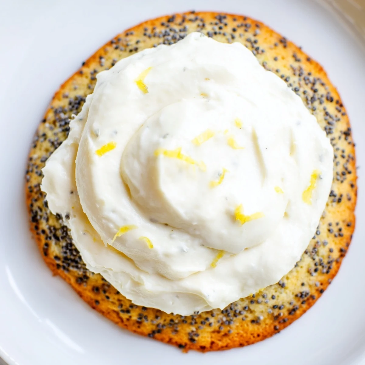 Buttery lemon poppy seed cookies with piped cream cheese frosting, garnished with fresh lemon zest on a wooden board