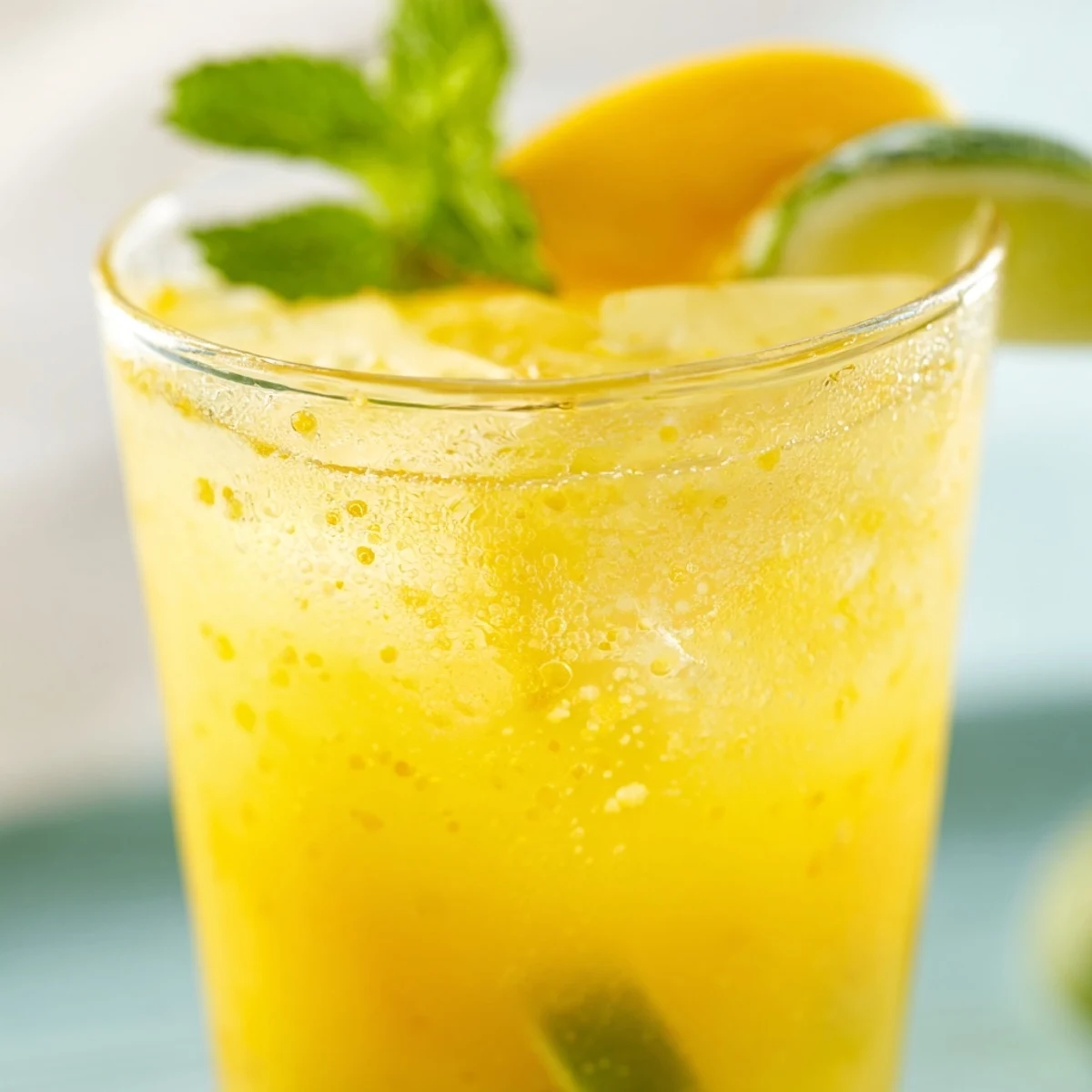 Golden mango ginger mocktail in a clear glass with ice and fresh mango slice garnish