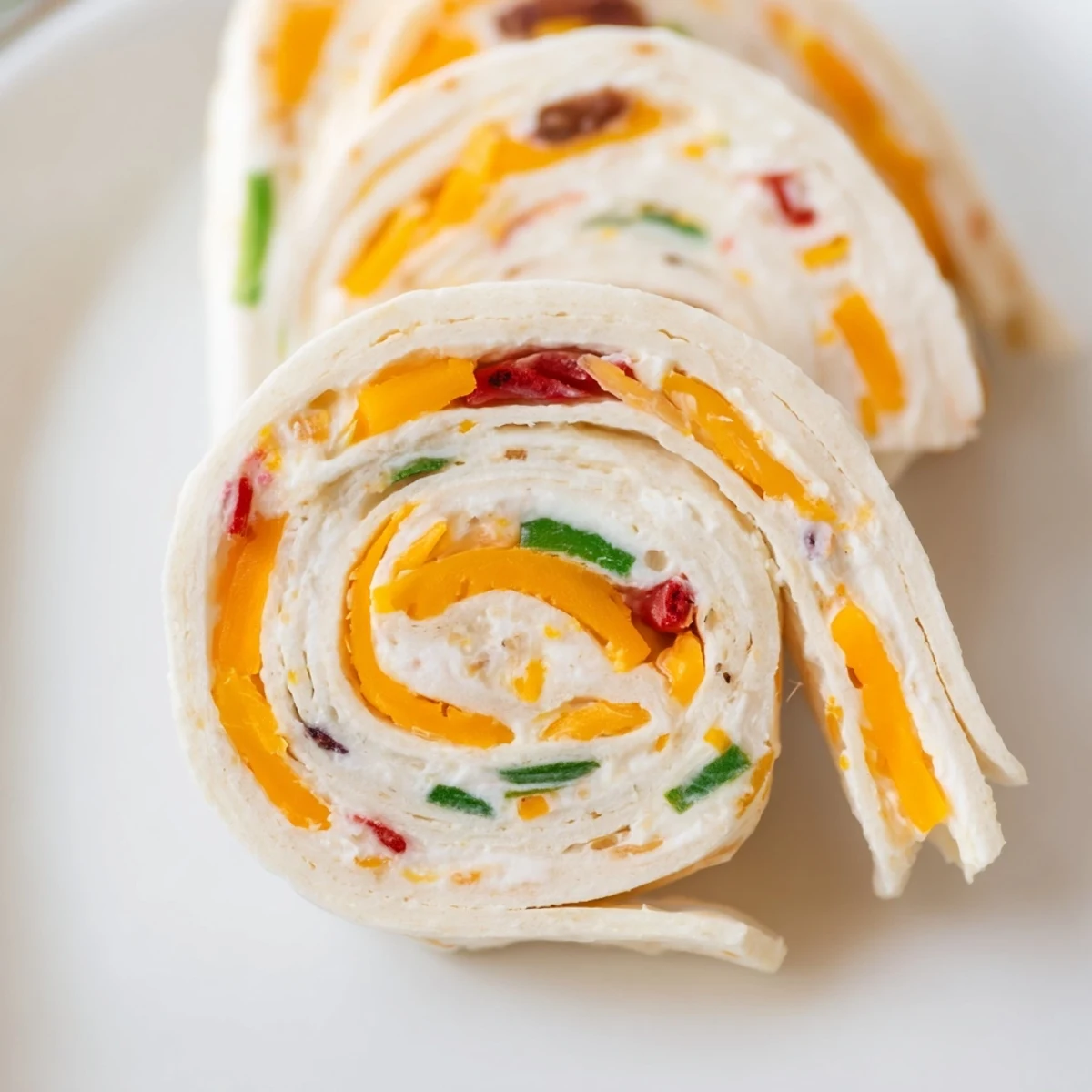 Close-up of sliced pinwheel appetizers showing red pepper, green onion, and cheddar cheese layers