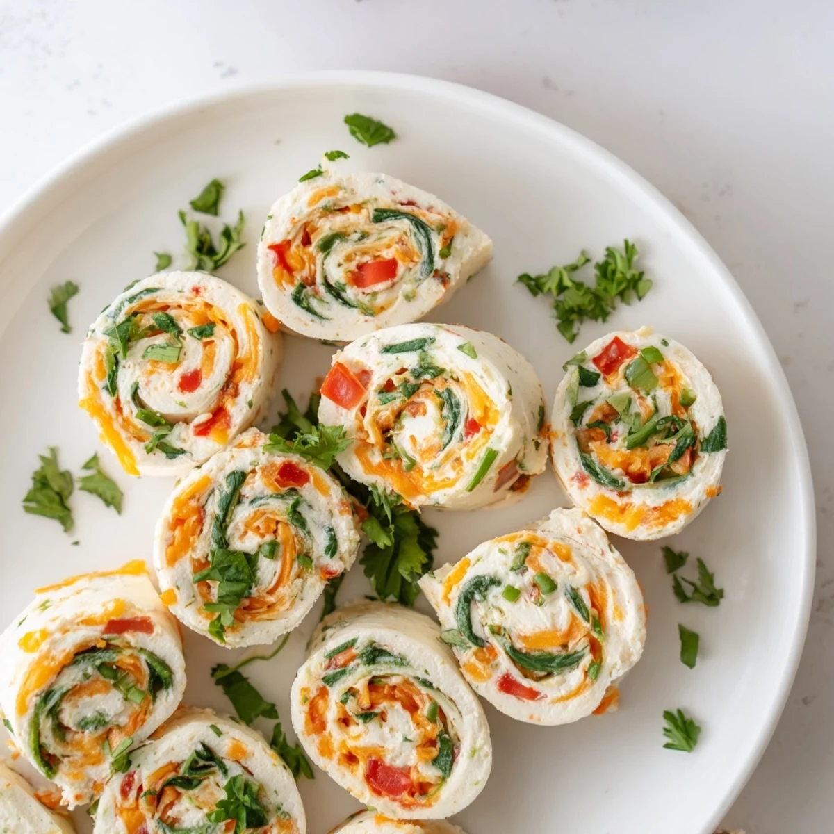 Golden swirls of cream cheese pinwheels arranged on a white serving platter with fresh parsley garnish