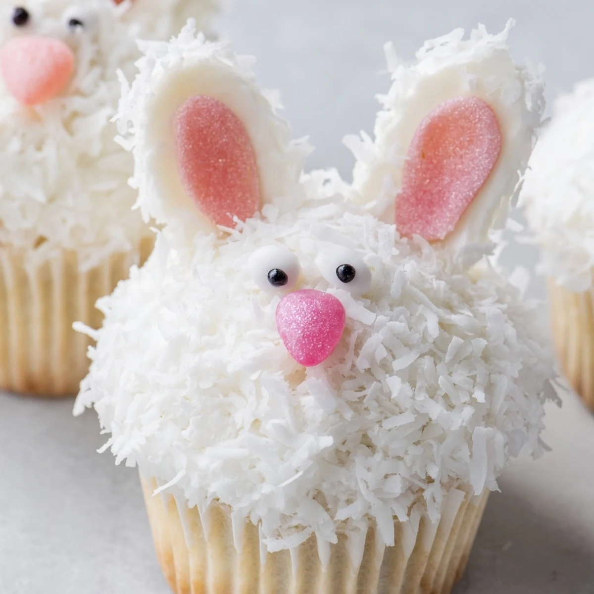 Adorable bunny cupcakes decorated with pink sugar ears and jelly bean noses on a white platter
