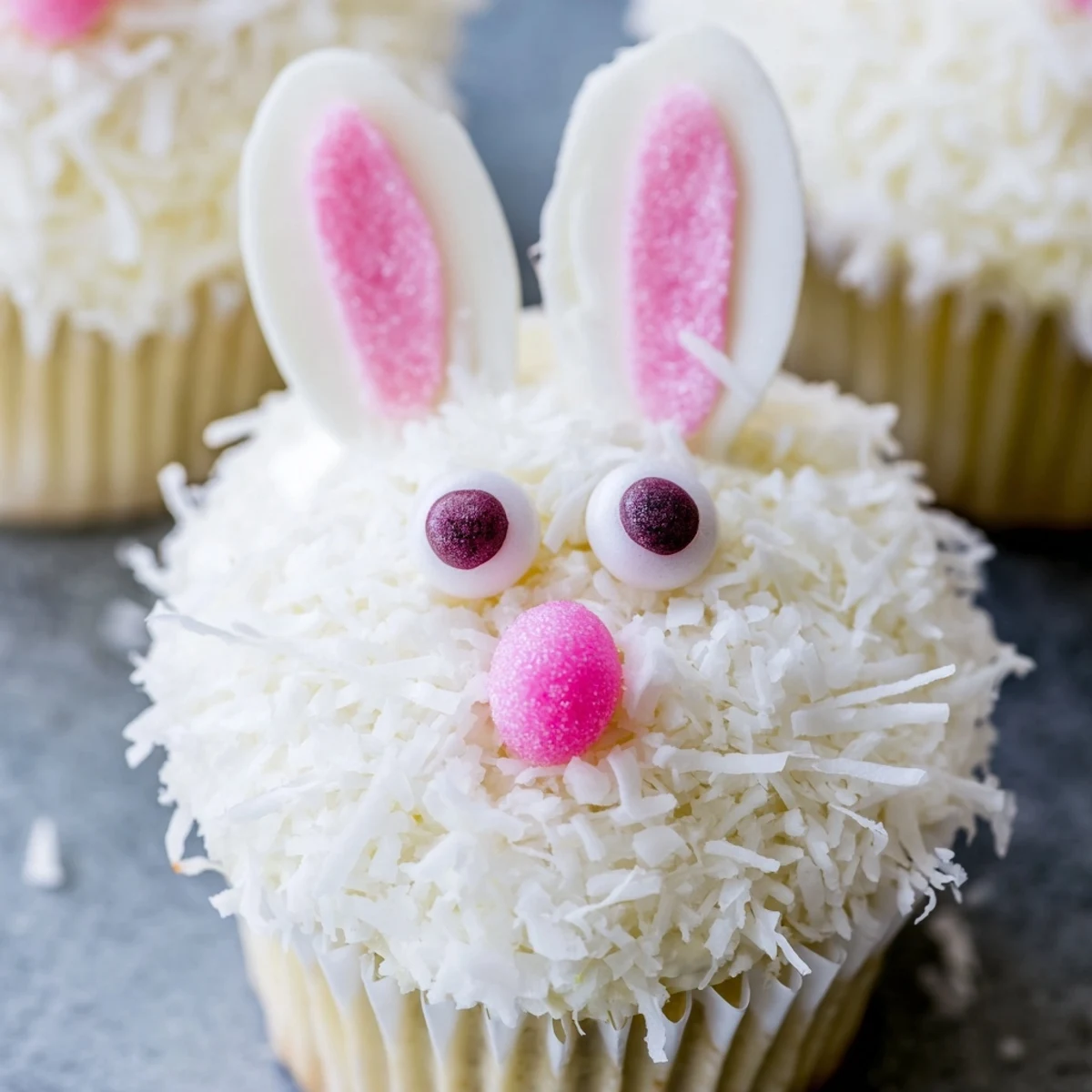 Easter dessert featuring vanilla cupcakes with coconut coating and cute marshmallow bunny ear decorations