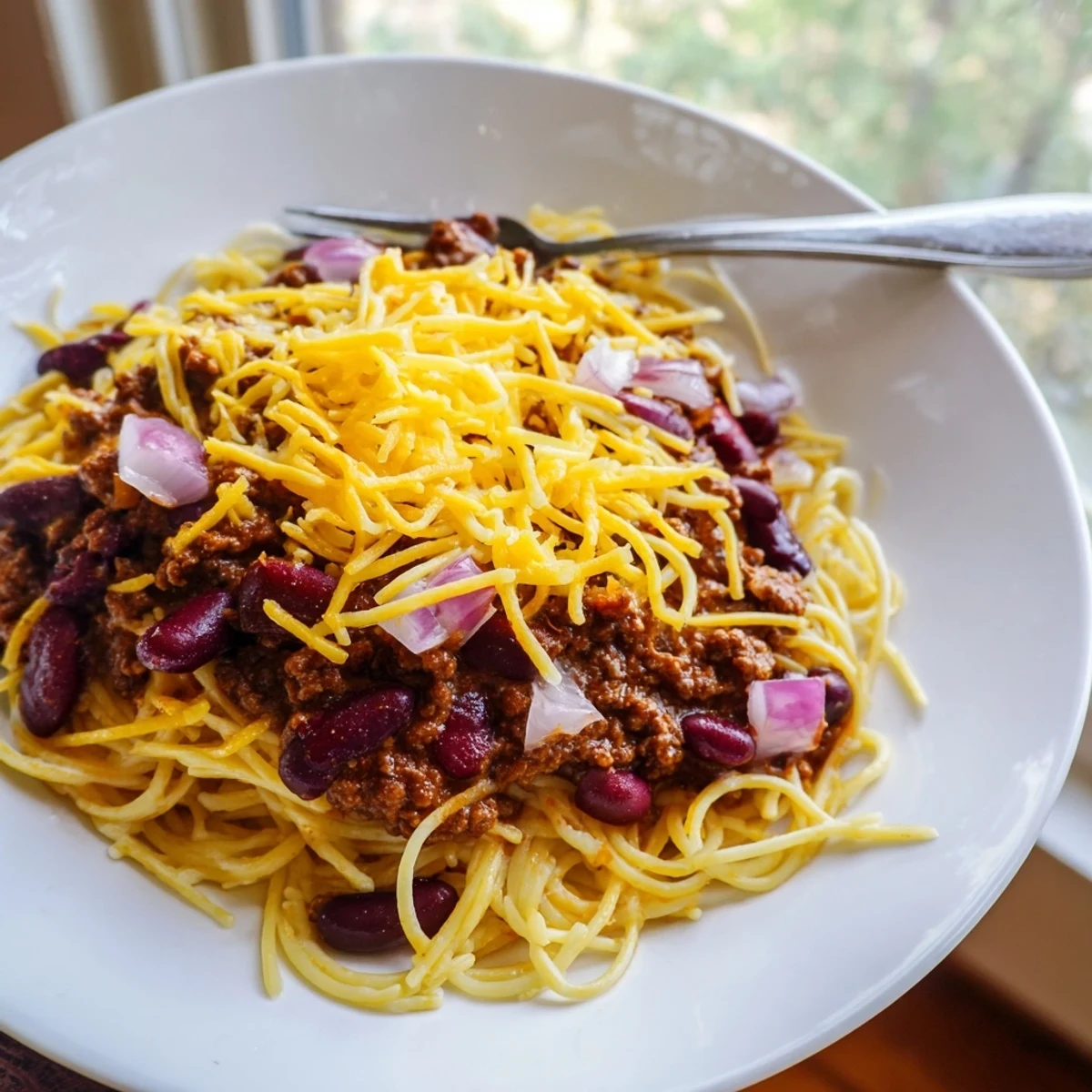 Homemade Cincinnati Chili served over spaghetti topped with melted cheddar cheese and diced onions