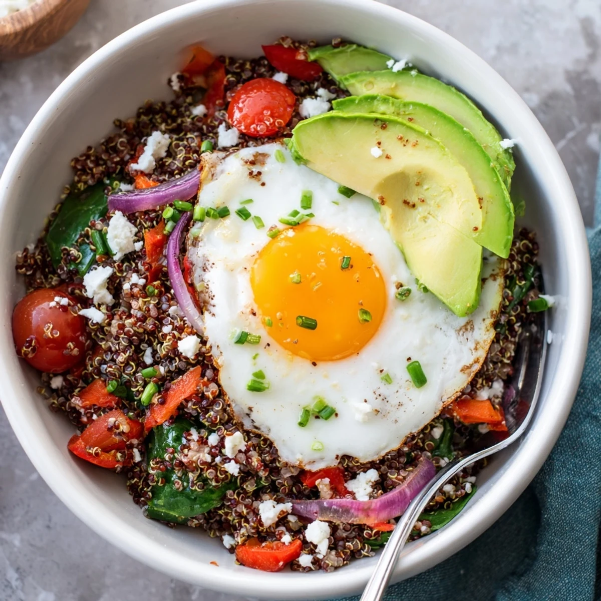 Golden fried egg rests atop fluffy savory quinoa breakfast bowl with sautéed colorful vegetables