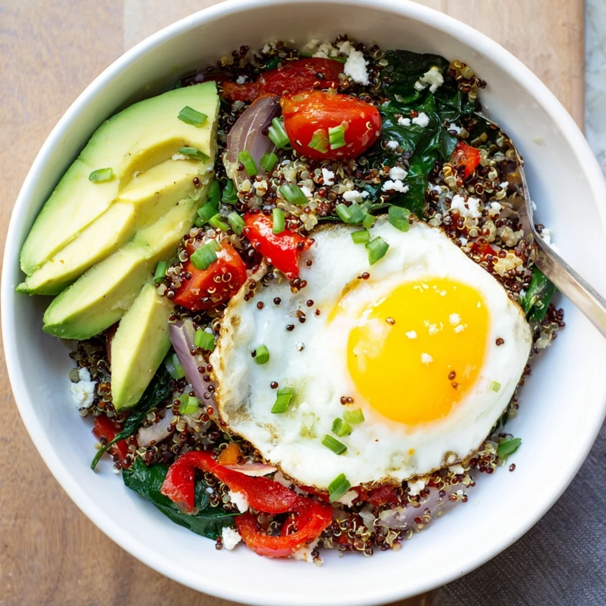 Protein-rich savory quinoa breakfast bowl featuring fried egg over tender vegetables and herbs