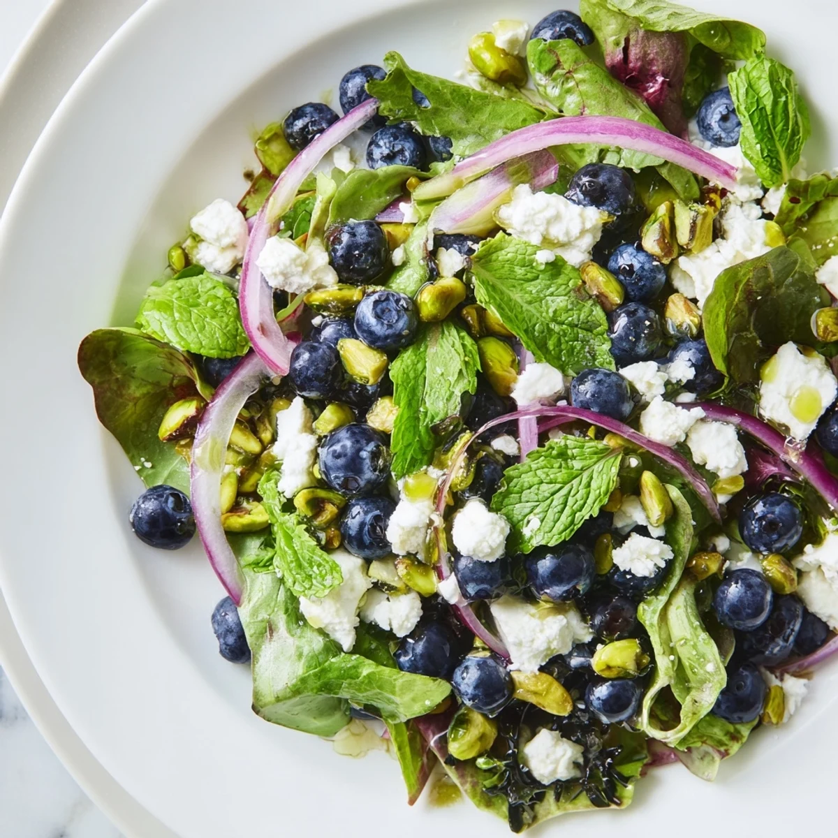 Blueberry Pistachio Spring Salad topped with crumbled feta cheese and glossy lemon honey vinaigrette