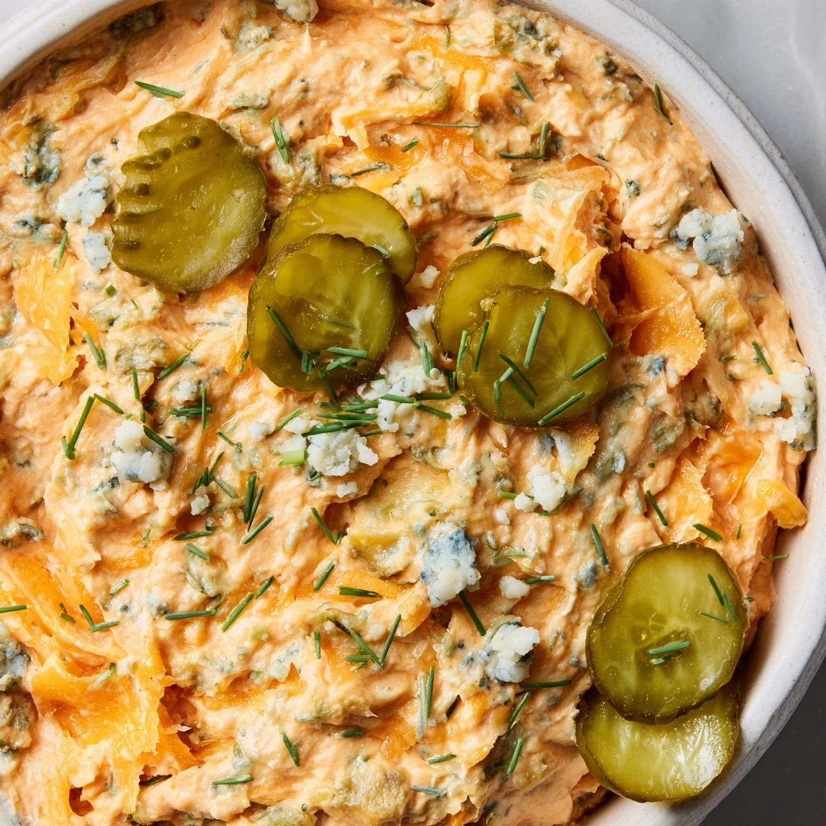 Tangy buffalo pickle dip topped with cheddar cheese and garnished with sliced pickles