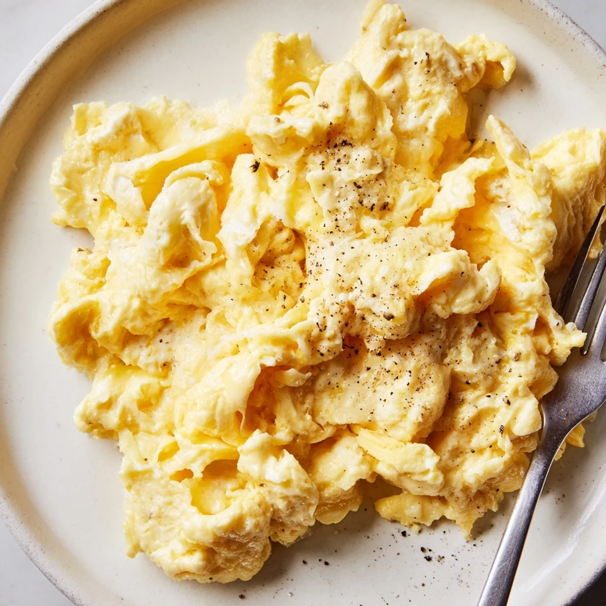 Soft curds of scrambled eggs topped with black pepper beside sliced avocado
