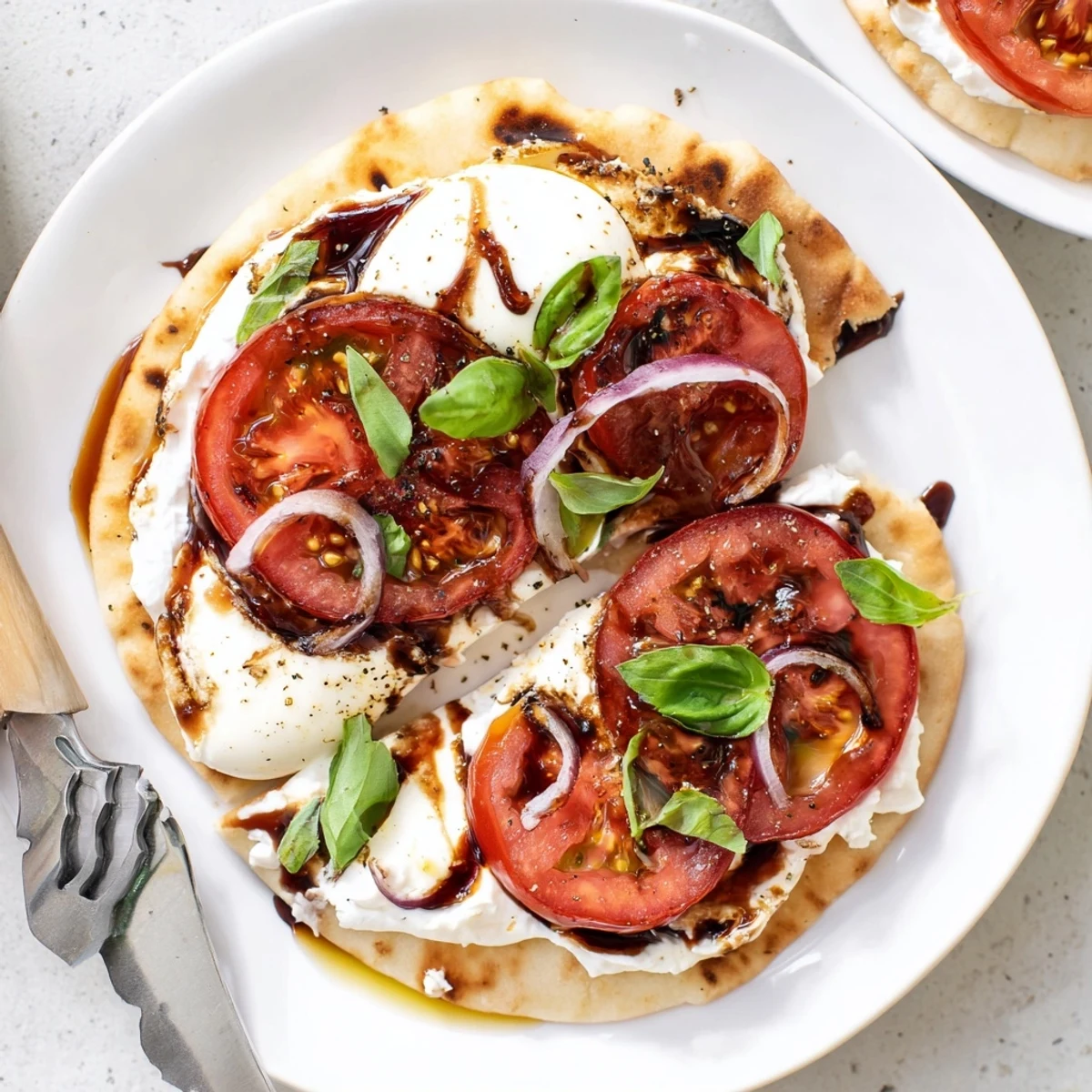 Sliced tomatoes, basil, and balsamic drizzle atop Caprese Pita Pizza With Whipped Garlic Feta