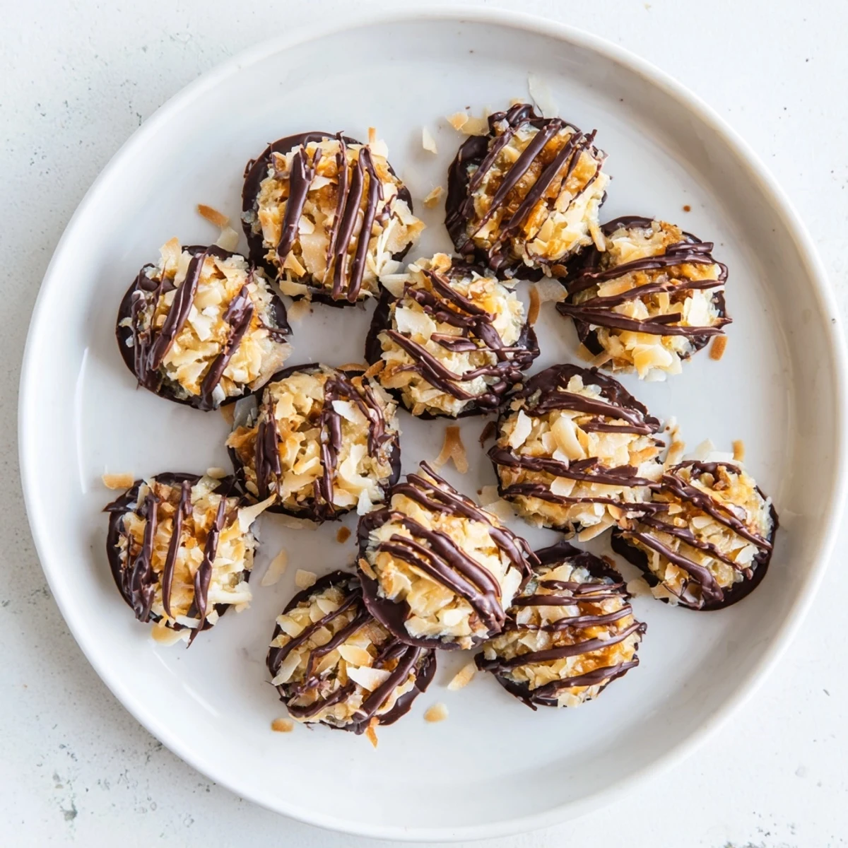 Golden no bake Samoa bites stacked on a white plate featuring chocolate drizzle and toasted coconut topping