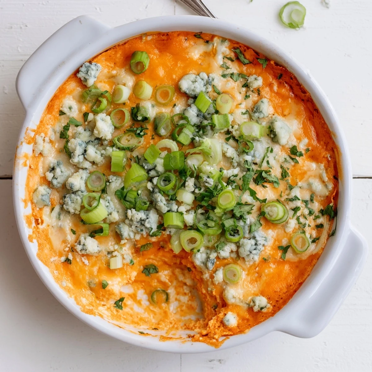 Golden cheesy white bean buffalo dip bubbling in a baking dish with melted cheddar and garnish