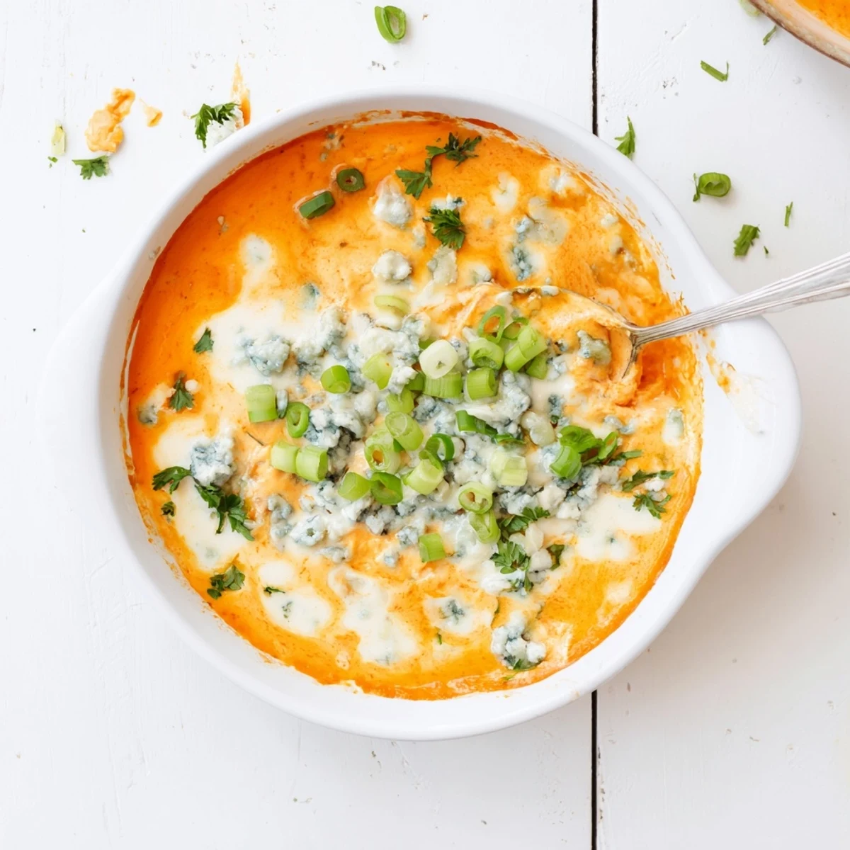 Spicy white bean buffalo appetizer with blue cheese crumbles and green onions atop a golden bubbling surface