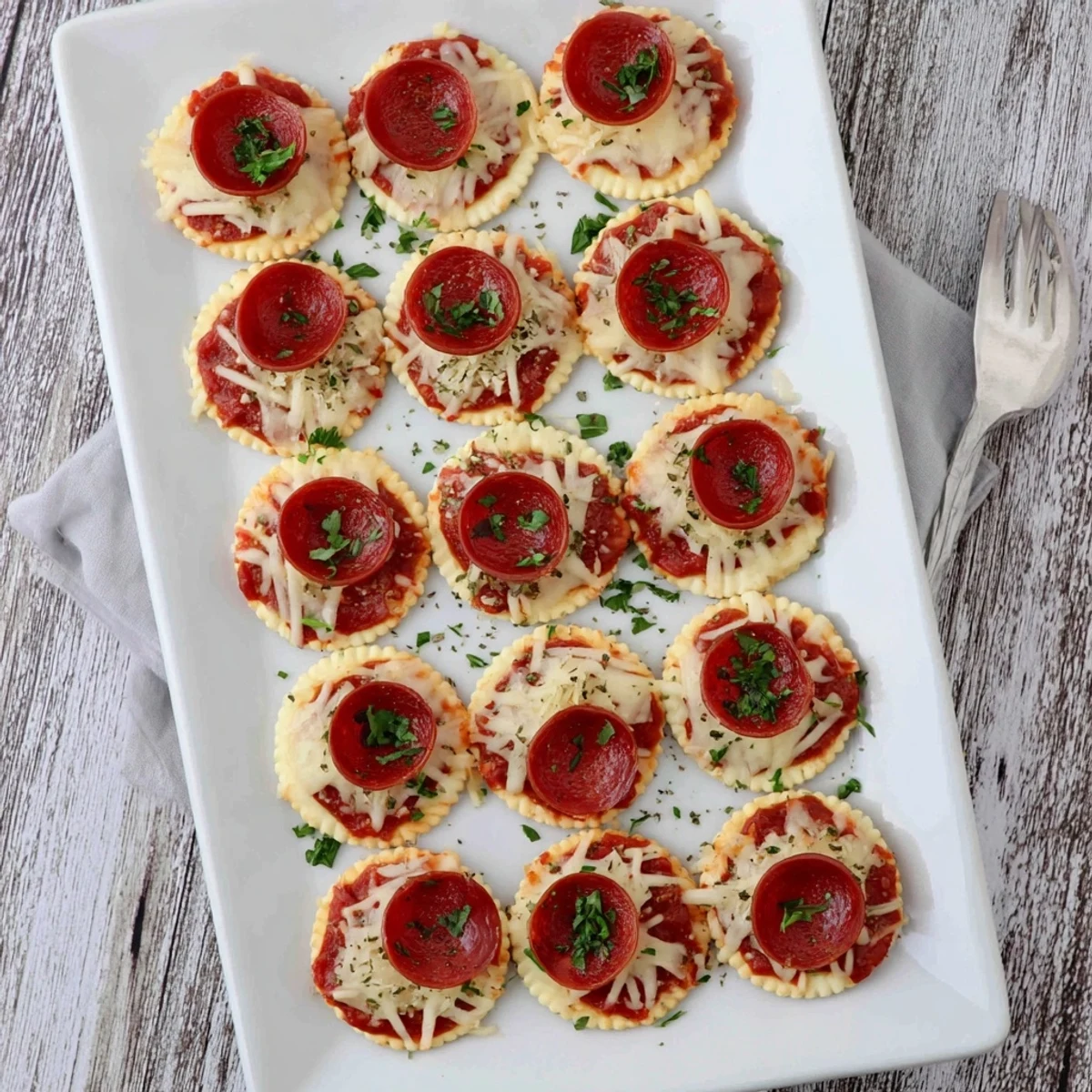 Bite-sized beef pepperoni pizza crackers garnished with parsley on a parchment-lined baking sheet