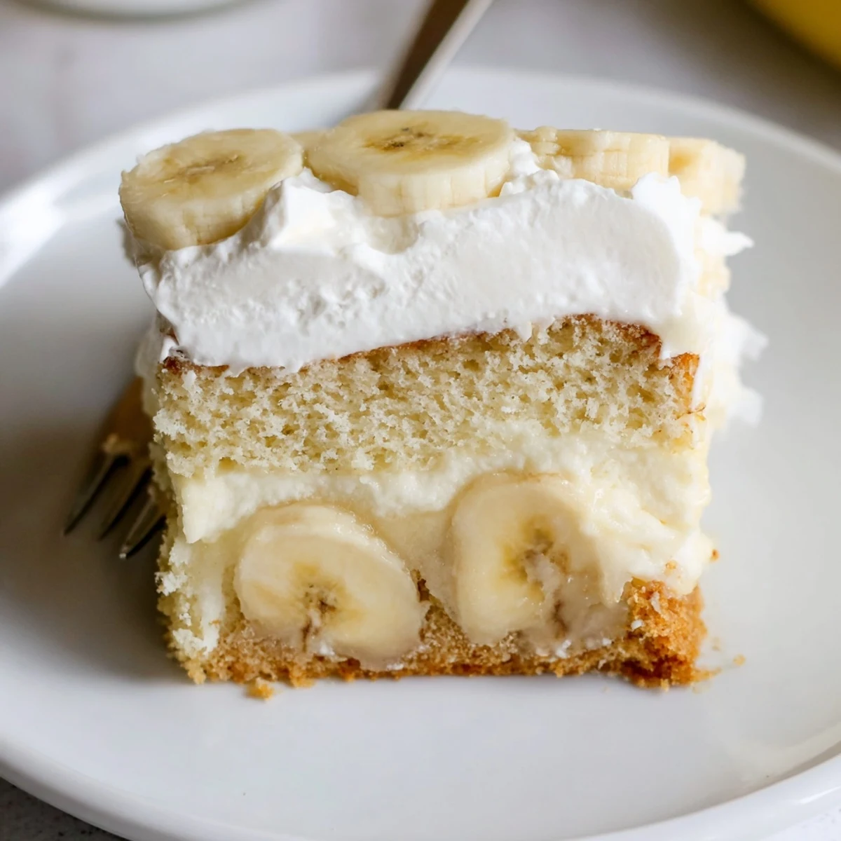 Slice of Banana Pudding Cake Recipe on plate, tender crumb and ripe banana rounds.