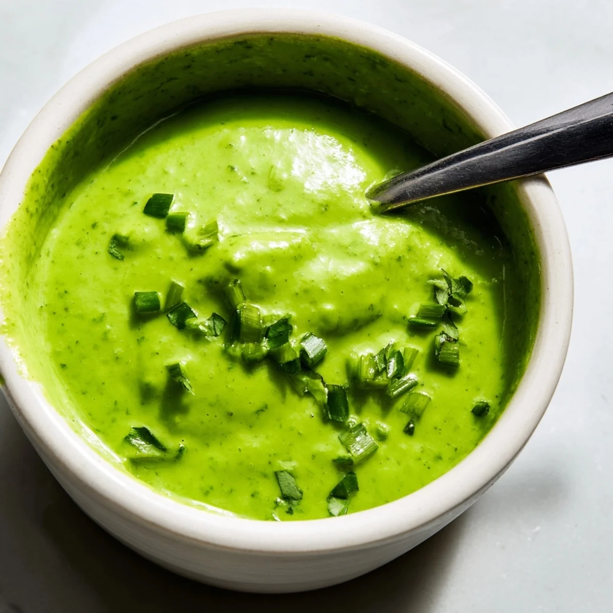 Vibrant bowl of spicy aji verde Peruvian green sauce garnished with extra green onions