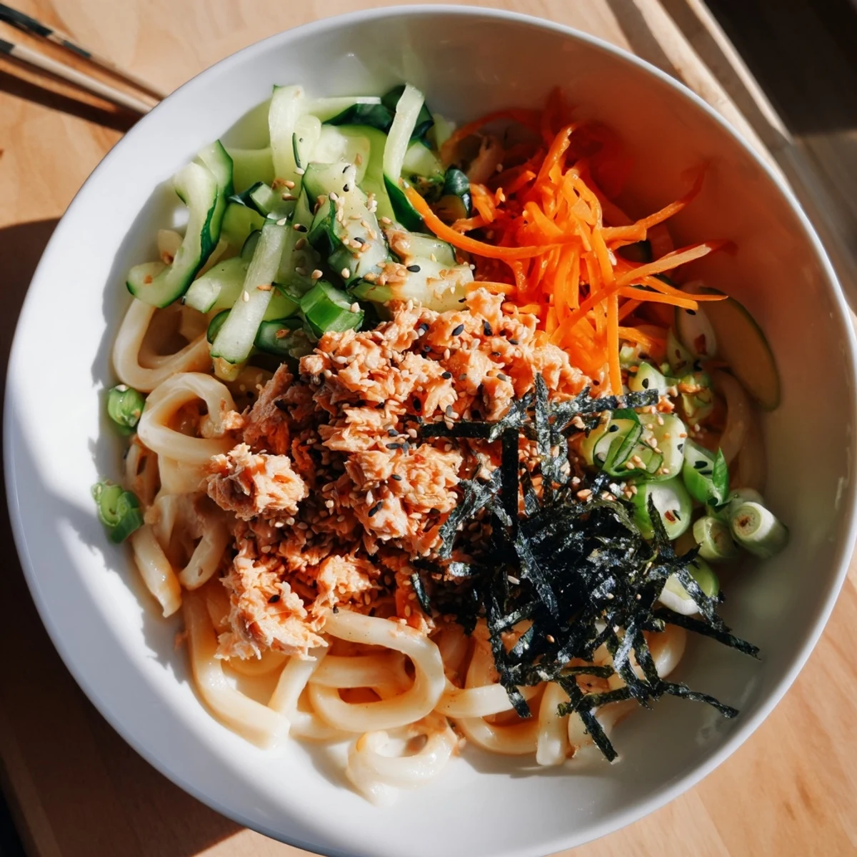 Steaming bowl of spicy tuna udon noodles tossed with vegetables and sesame seeds