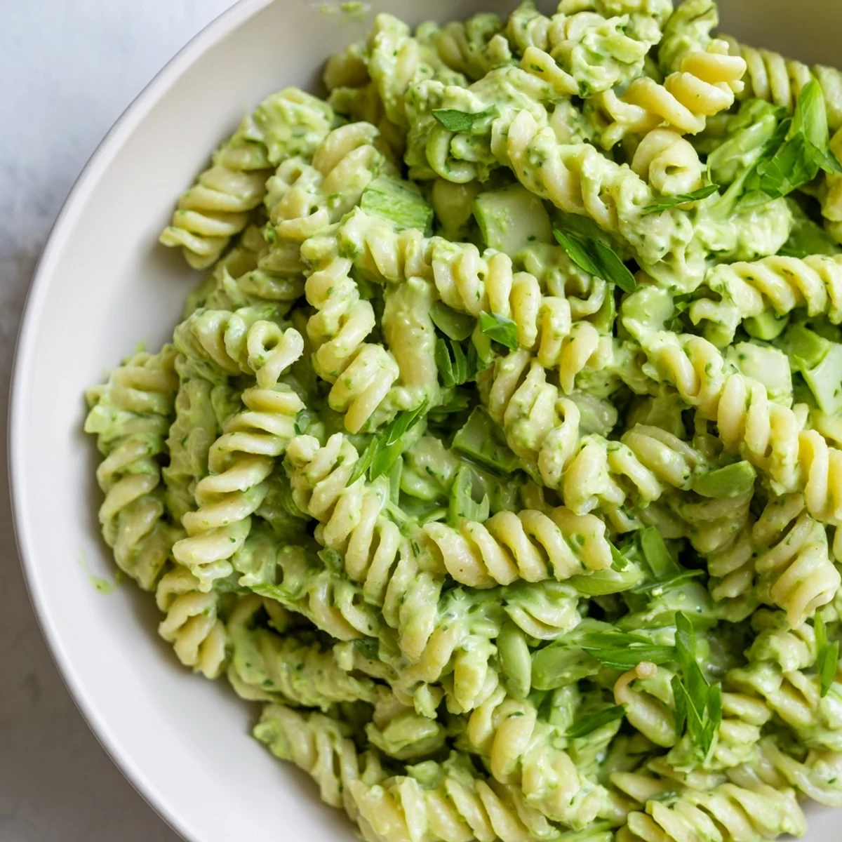 A bowl of Green Goddess Pasta Salad gleaming with herbaceous green dressing and seeds.
