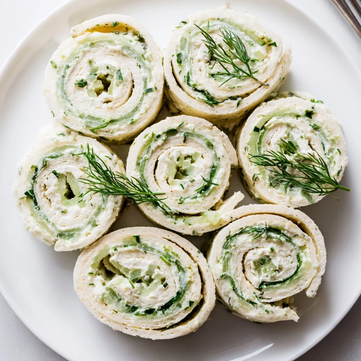 Party-ready Cucumber And Dill Pinwheels rolled in tortillas, chilled, garnished with dill