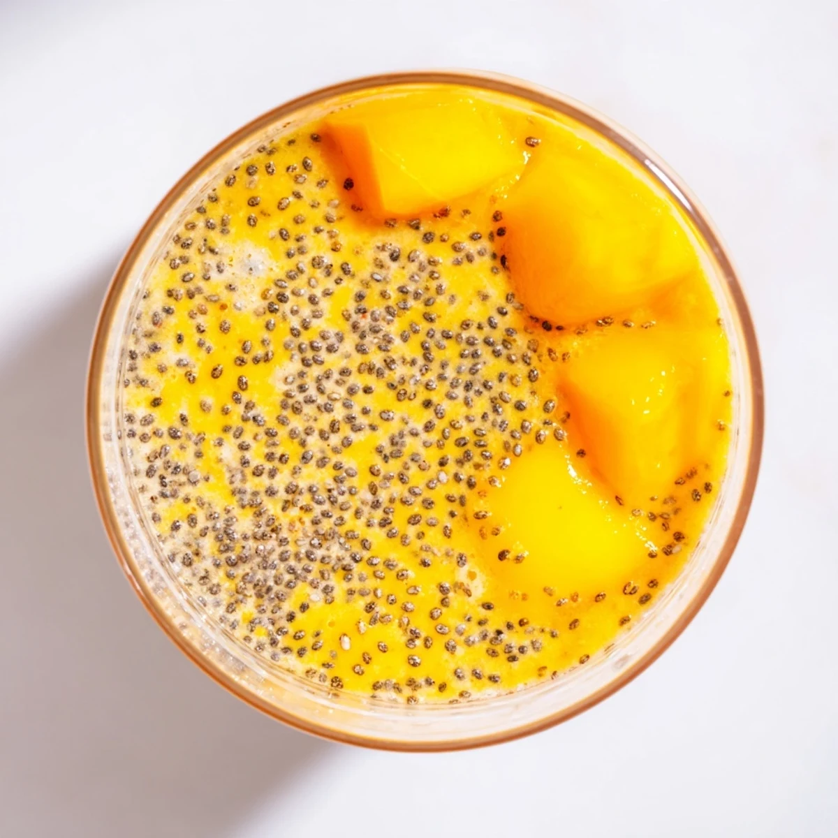 Thick Tropical Sunrise Protein Smoothie poured into a glass with fresh fruit garnish