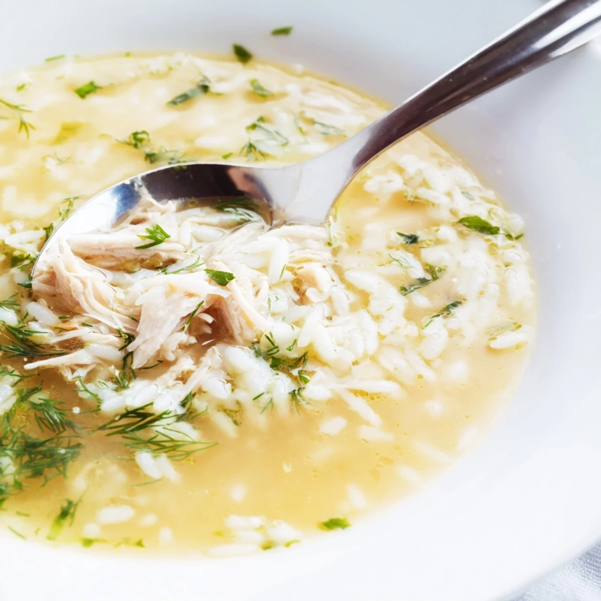 Creamy Greek lemon chicken soup featuring tender chunks of chicken and fluffy rice in a bright yellow broth