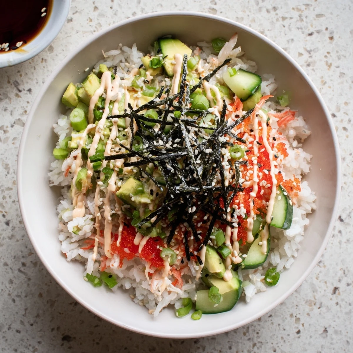 Colorful California Roll sushi bowl topped with avocado, crab, cucumber, and drizzled spicy mayo