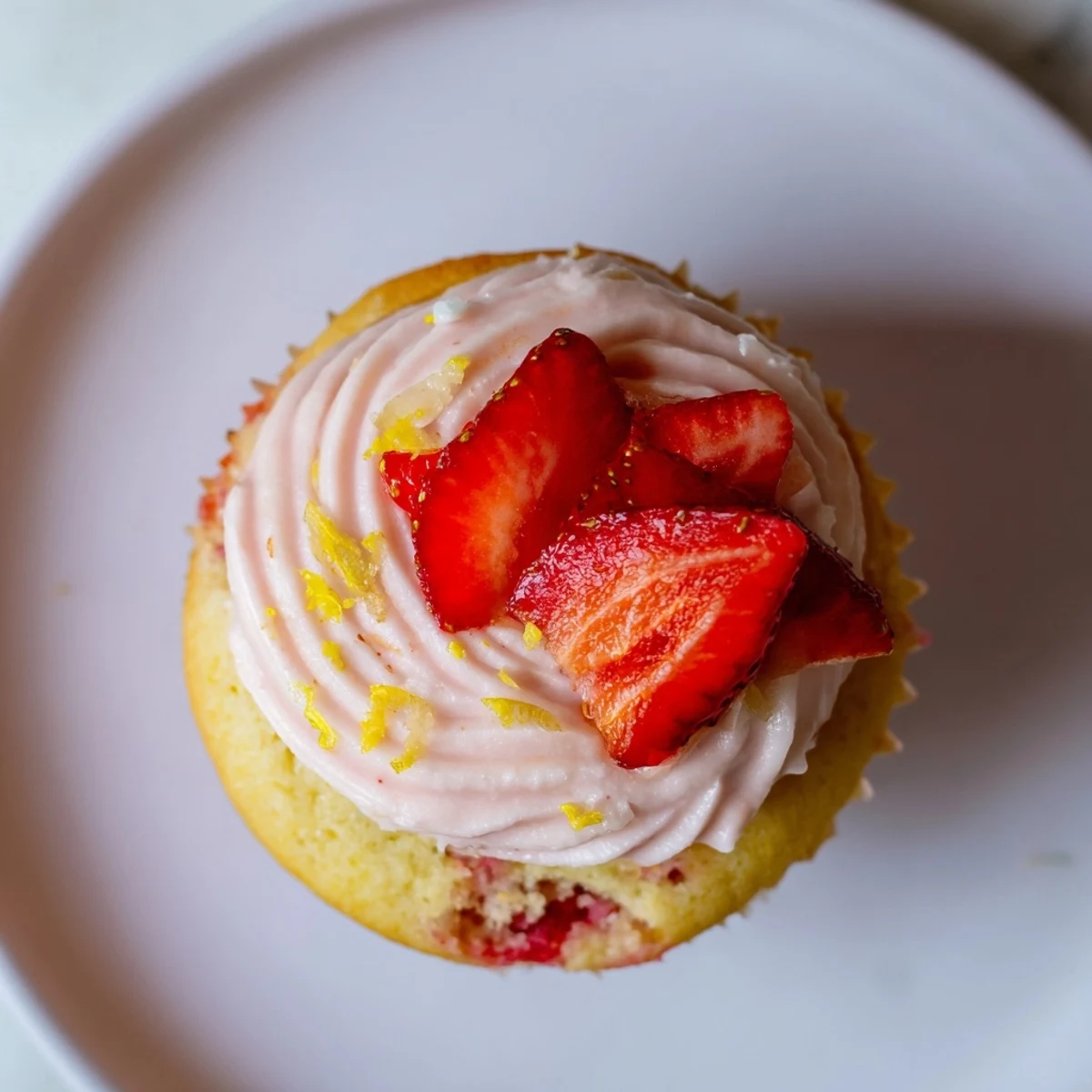 Freshly baked strawberry lemonade cupcakes topped with pink buttercream and garnished with strawberry slices